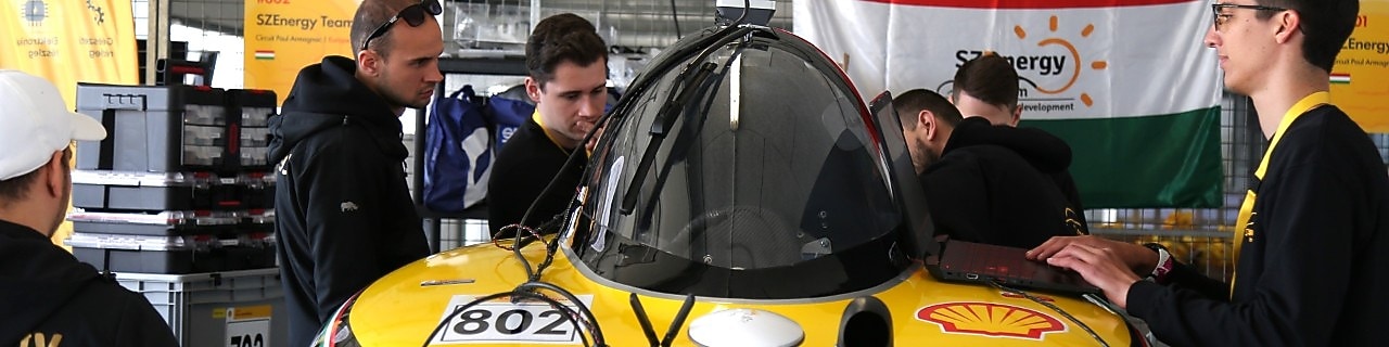a group of students working on a yellow vehicle inside a paddock
