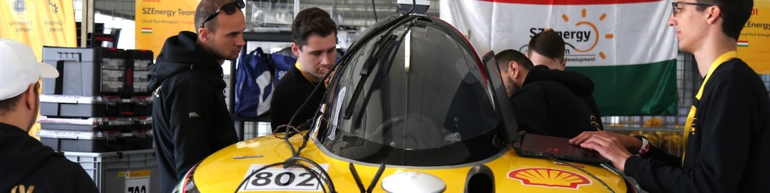 a group of students working on a yellow vehicle inside a paddock