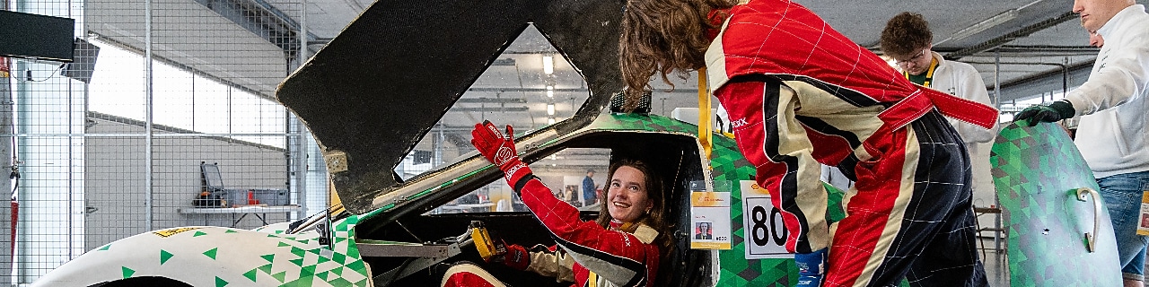 A young person riding inside a homemade vehicle, talking to another person standing beside the car