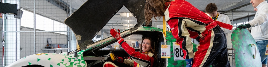 A young person riding inside a homemade vehicle, talking to another person standing beside the car