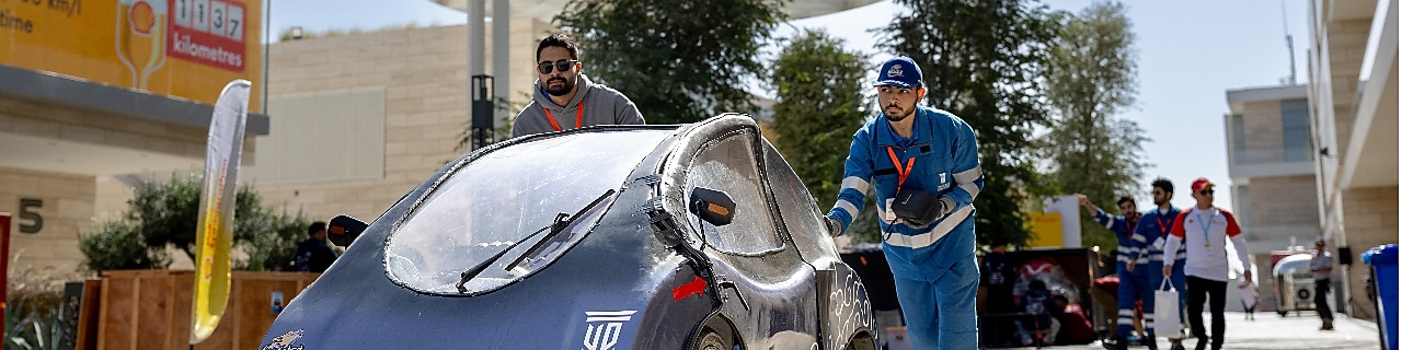 Two young persons pushing a prototype vehicle in the pit lane of a track