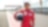 a young person wearing a driving suit and holding a race helmet posing in the pit lane of a race track