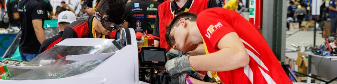 two young people wearing glasses, gloves working on a self-made car engine in Brazil competition