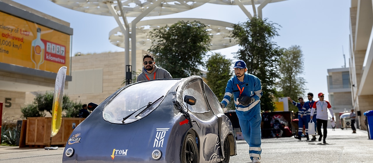 Two young persons pushing a prototype vehicle in the pit lane of a track