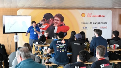 Person in blue holding a microphone, presenting a lecture to an audience of young people