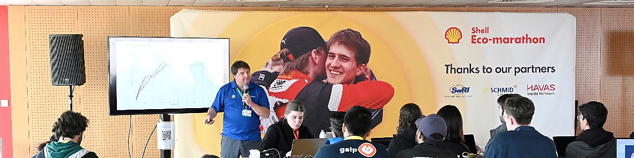 Person in blue holding a microphone, presenting a lecture to an audience of young people