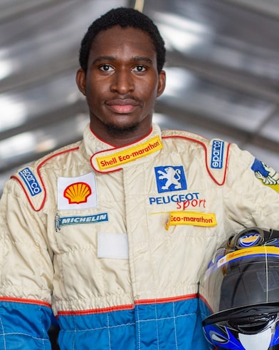 A person in a race car suit holding a helmet