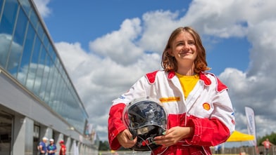 A person in a red and white race suit suit holding a helmet