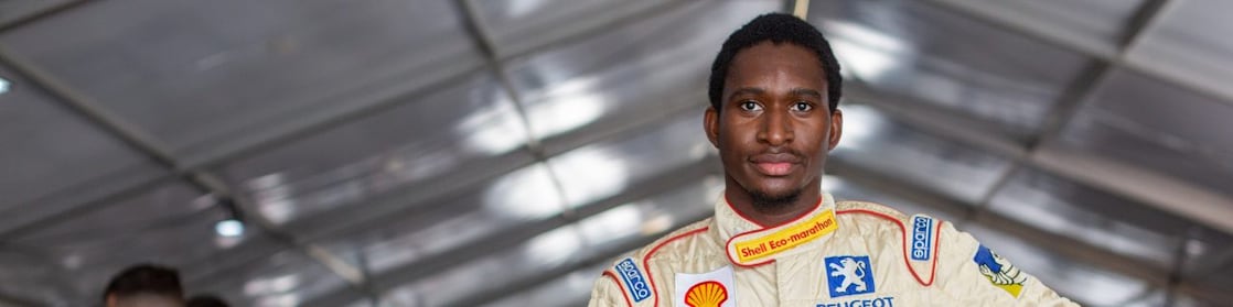 A person in a race car suit holding a helmet