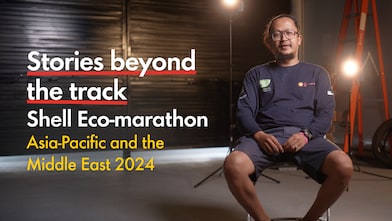 a young person seated inside a racetrack paddock, studio lights behind them