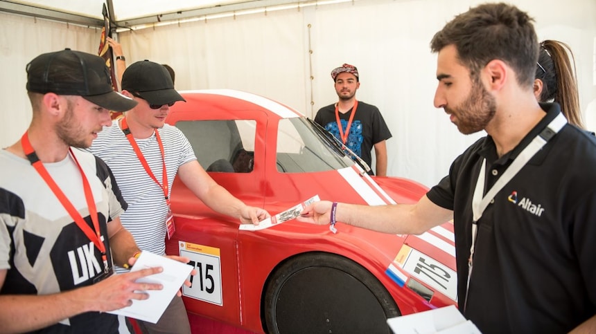Men stand round a red car