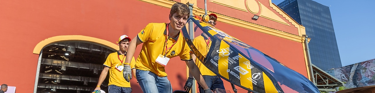 A young person smiling while pushing a self-made car