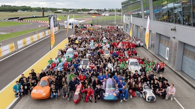 A group of people and prototype vehicles standing together at an race track