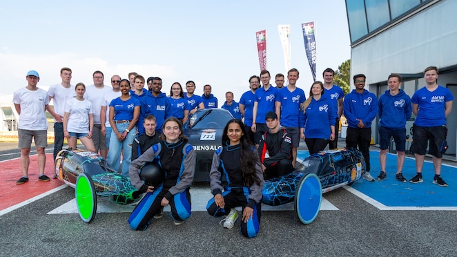 A group of young people posing in front of prototype cars on the track
