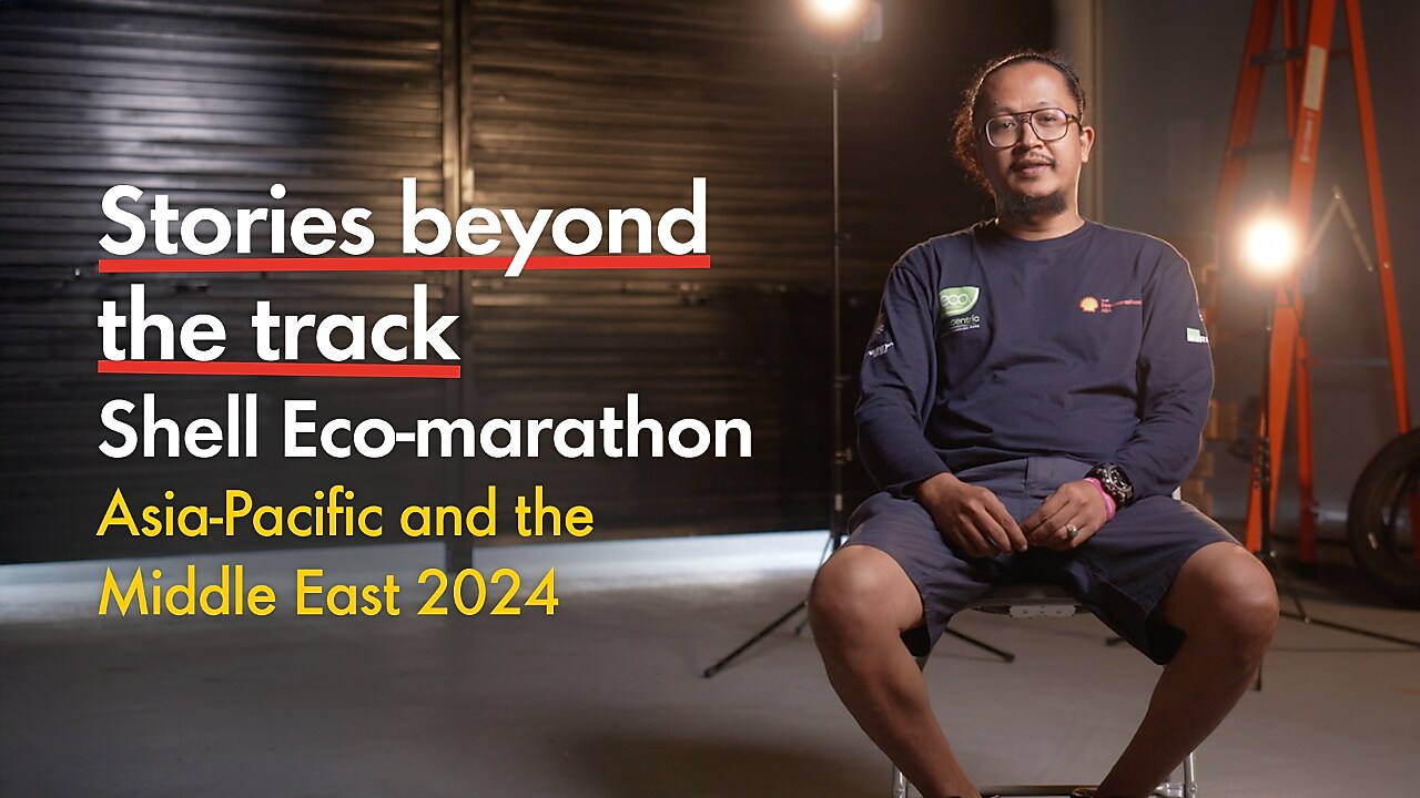 a young person seated inside a racetrack paddock, studio lights behind them