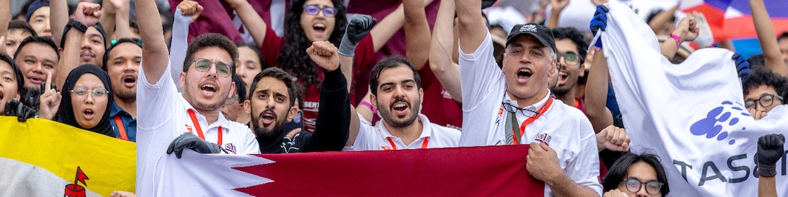 A group of young people holding the Qatar flag in a crowd